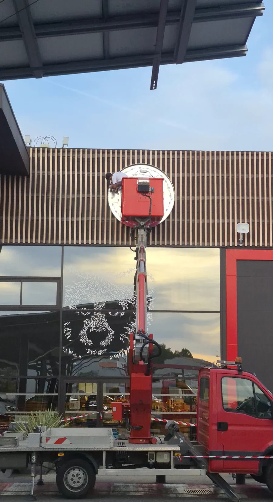 Pose d'une enseigne ronde lumineuse en nacelle sur le bandeau bois d'une façade.
